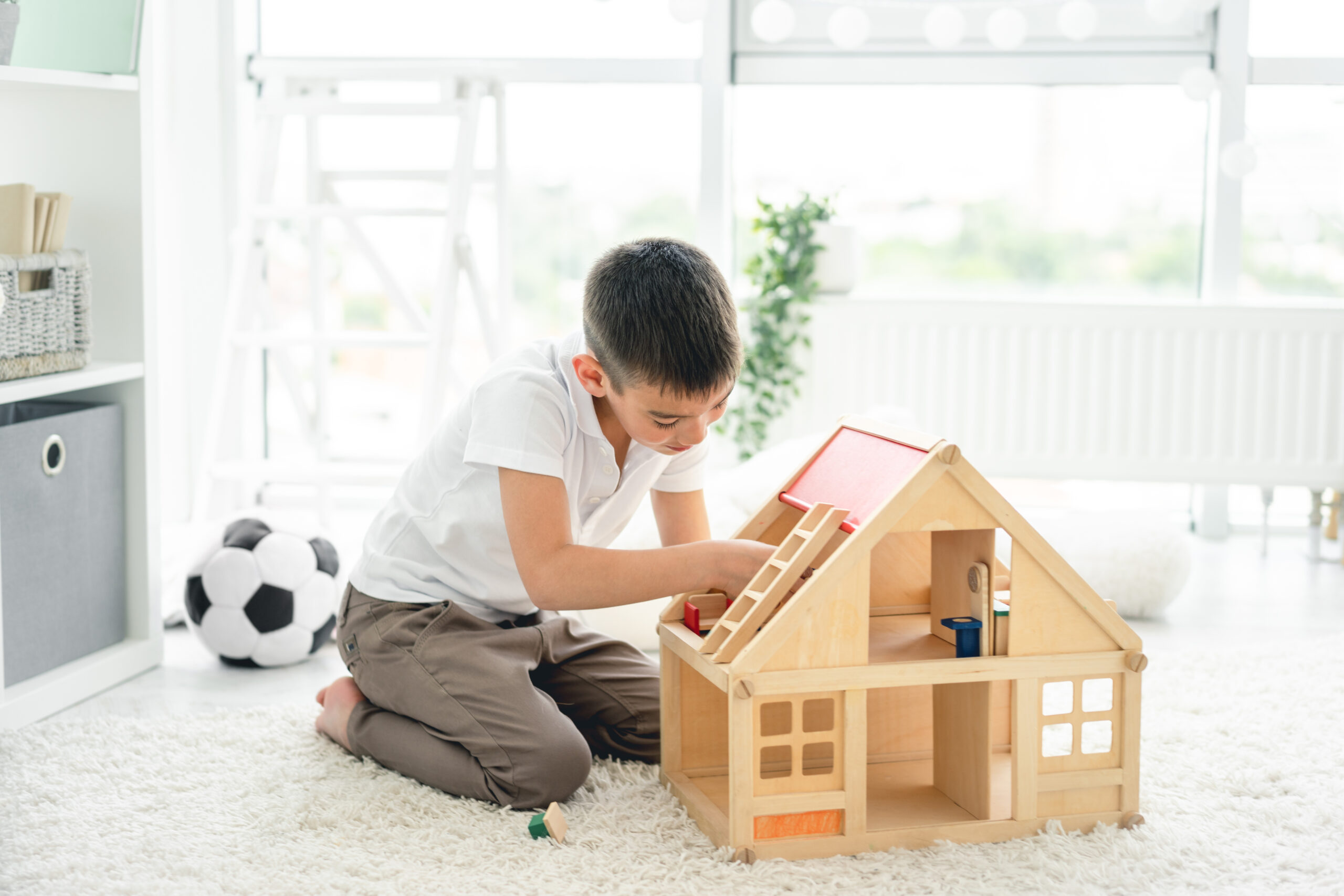 little boy playing alone with wooden house in kids room